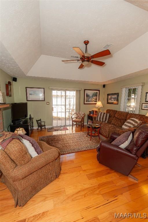 living room featuring ceiling fan, a raised ceiling, a textured ceiling, and light wood-type flooring