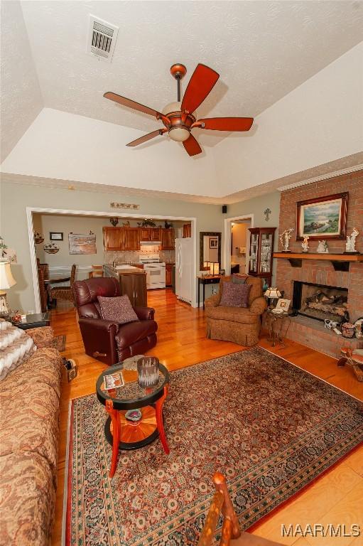 living room with hardwood / wood-style flooring, a brick fireplace, lofted ceiling, and a tray ceiling