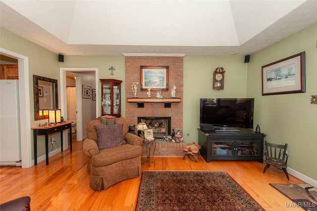 living room featuring a brick fireplace, light hardwood / wood-style flooring, a raised ceiling, and a textured ceiling