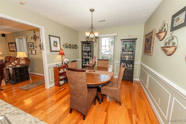 dining area with a notable chandelier, light hardwood / wood-style flooring, and a textured ceiling