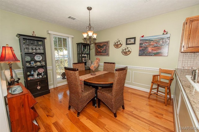 dining room with a textured ceiling, a chandelier, and light wood-type flooring