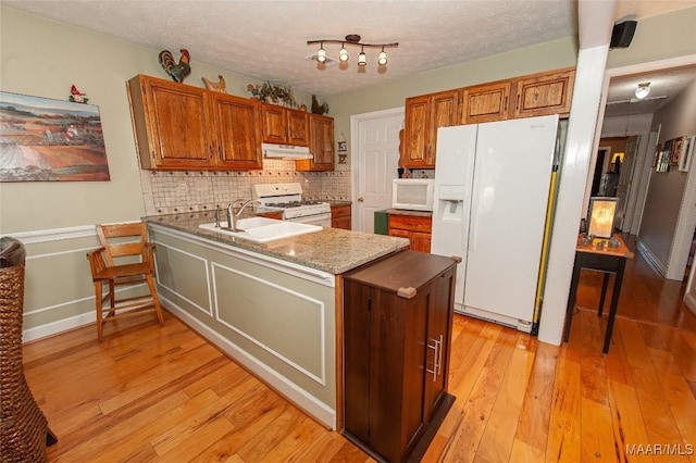 kitchen with sink, white appliances, backsplash, a textured ceiling, and light wood-type flooring