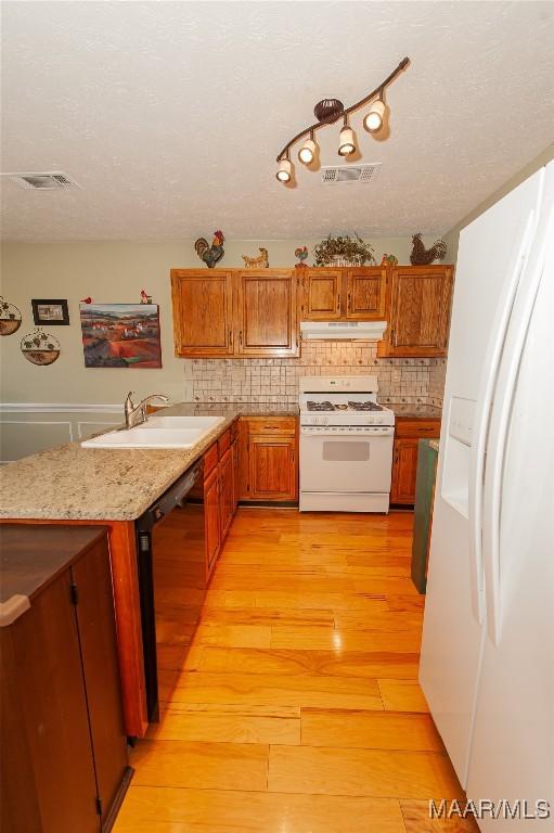 kitchen with sink, light wood-type flooring, backsplash, white appliances, and a textured ceiling