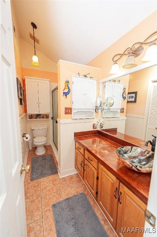 bathroom with lofted ceiling, a shower with door, tile patterned flooring, vanity, and toilet