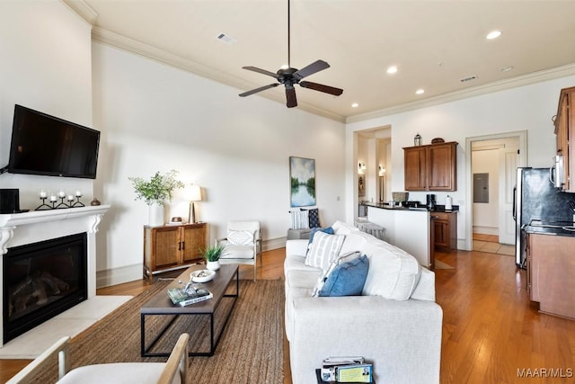 living room with ceiling fan, ornamental molding, electric panel, and light hardwood / wood-style floors