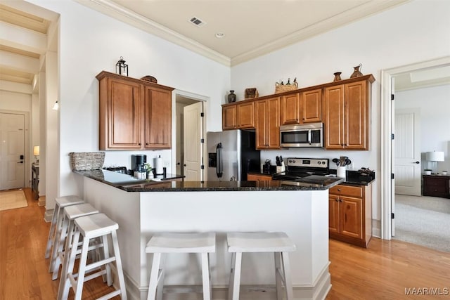 kitchen with crown molding, appliances with stainless steel finishes, dark stone countertops, a kitchen breakfast bar, and light hardwood / wood-style floors