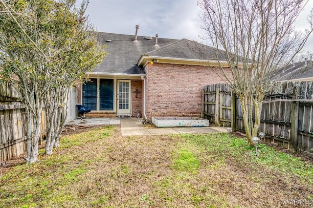 back of house with a shingled roof, brick siding, a lawn, and a fenced backyard