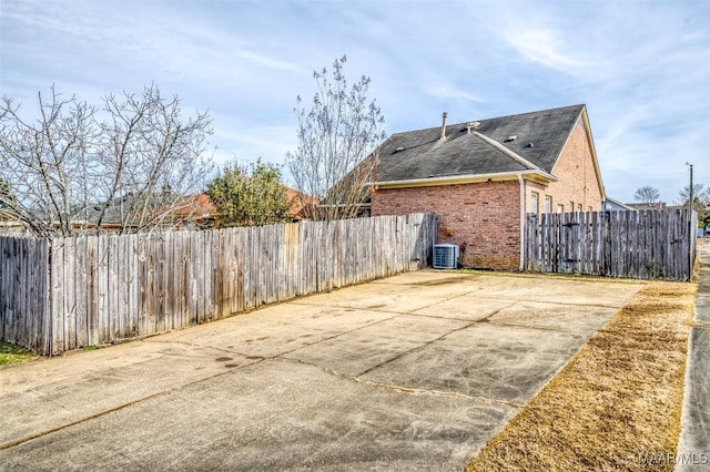 view of side of property featuring fence, central AC unit, a patio, and brick siding