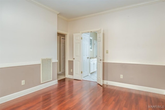 spare room featuring ornamental molding, visible vents, baseboards, and wood finished floors