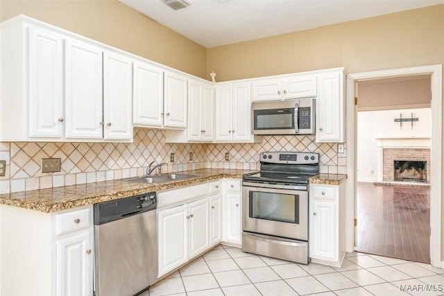 kitchen with light tile patterned floors, stainless steel appliances, a sink, white cabinetry, and backsplash