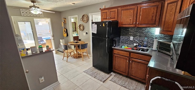 kitchen with light tile patterned flooring, tasteful backsplash, sink, ceiling fan, and black fridge