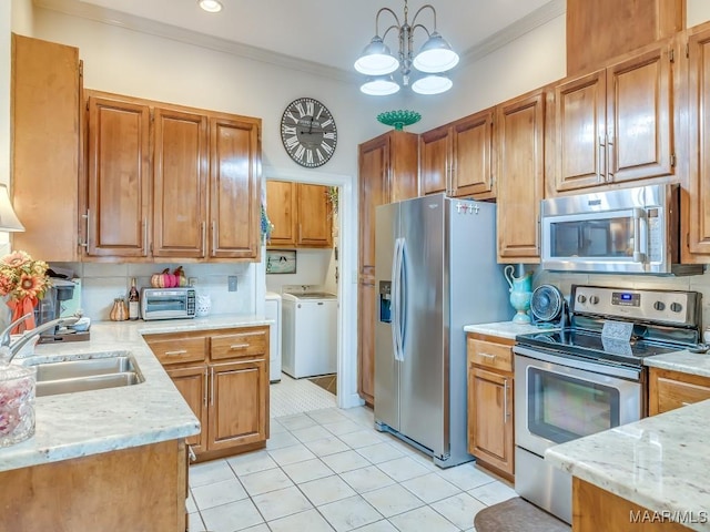 kitchen with sink, crown molding, washer and dryer, pendant lighting, and stainless steel appliances