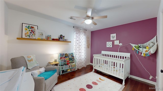 bedroom with wood-type flooring, a nursery area, and ceiling fan