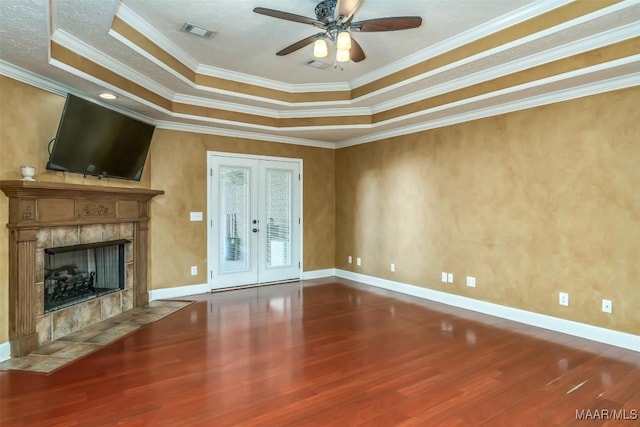 unfurnished living room with hardwood / wood-style flooring, a tray ceiling, a fireplace, ornamental molding, and french doors