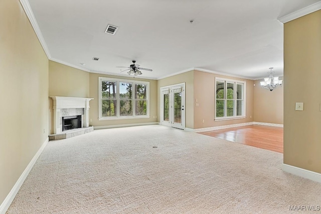 unfurnished living room with crown molding, light colored carpet, ceiling fan with notable chandelier, and a tile fireplace