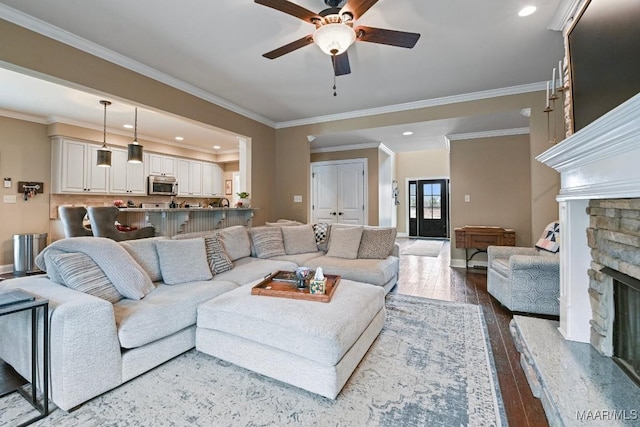 living room with hardwood / wood-style floors, a stone fireplace, ornamental molding, and ceiling fan