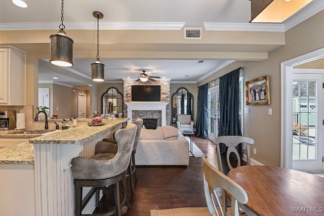 kitchen featuring a breakfast bar area, dark wood-type flooring, light stone counters, ornamental molding, and decorative light fixtures