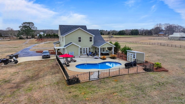 view of pool with a storage shed, a lawn, a patio area, and a rural view