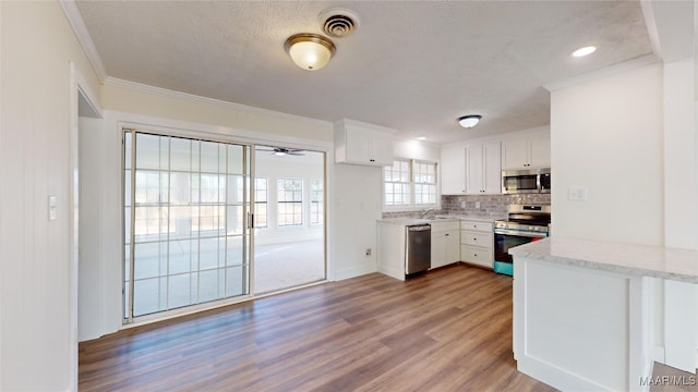 kitchen featuring hardwood / wood-style floors, sink, white cabinets, ornamental molding, and stainless steel appliances