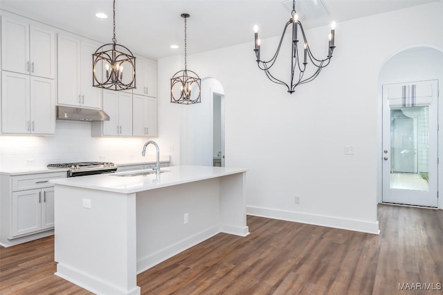 kitchen with decorative light fixtures, white cabinetry, sink, backsplash, and a kitchen island with sink