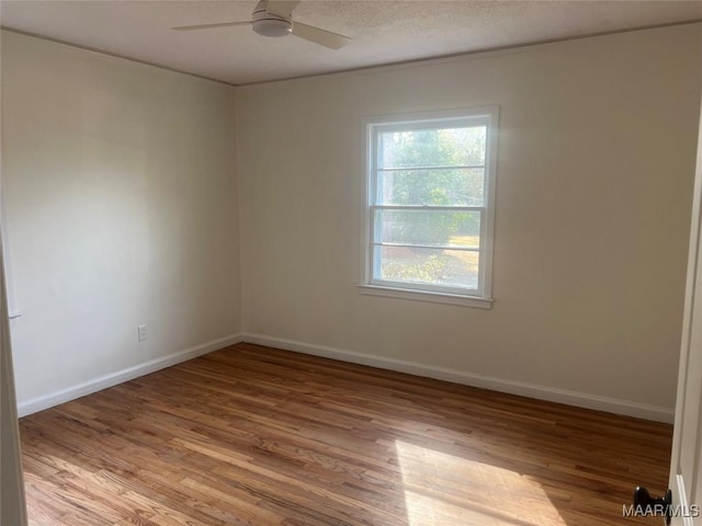 empty room with a textured ceiling, a ceiling fan, light wood-style flooring, and baseboards