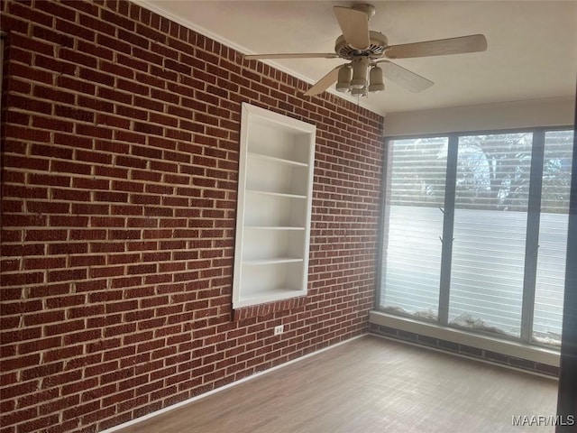 unfurnished room with built in shelves, plenty of natural light, brick wall, and wood finished floors