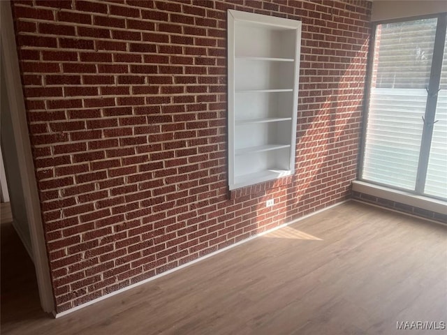 empty room with brick wall, built in features, and wood finished floors