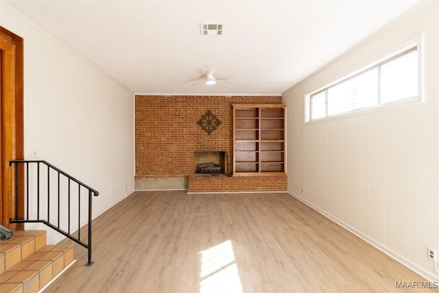 unfurnished living room featuring a fireplace, visible vents, a ceiling fan, ornamental molding, and wood finished floors