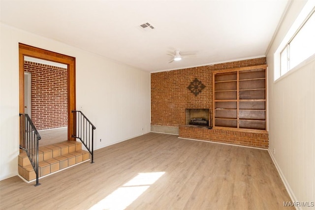 unfurnished living room featuring brick wall, a brick fireplace, wood finished floors, and visible vents