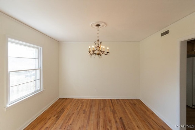 spare room with an inviting chandelier, baseboards, visible vents, and wood finished floors