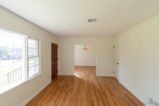 spare room featuring light wood-style flooring, visible vents, a chandelier, and baseboards