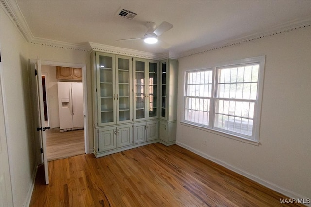 empty room with crown molding, baseboards, visible vents, and light wood-style floors