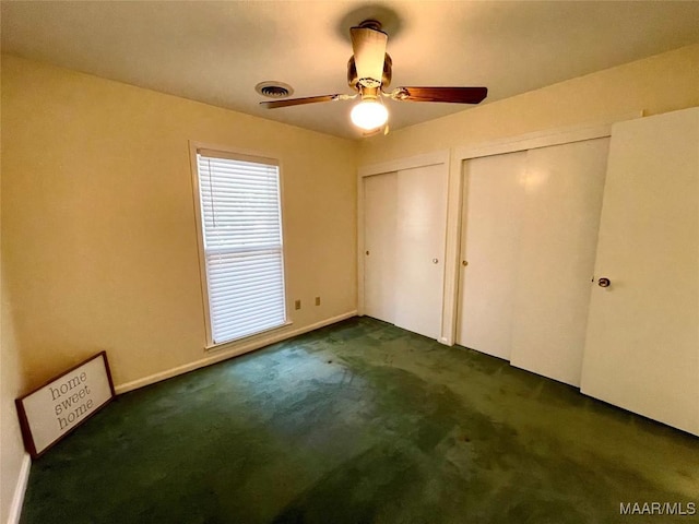 unfurnished bedroom featuring ceiling fan, two closets, and dark carpet