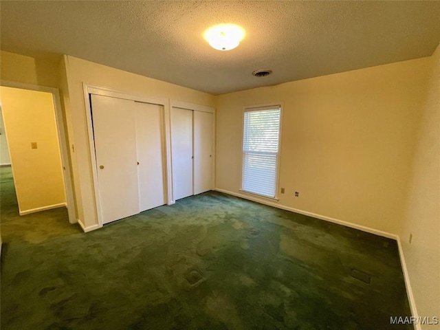 unfurnished bedroom featuring a textured ceiling, multiple closets, and dark colored carpet