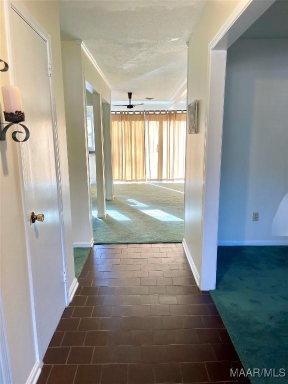 hall featuring a textured ceiling and dark colored carpet