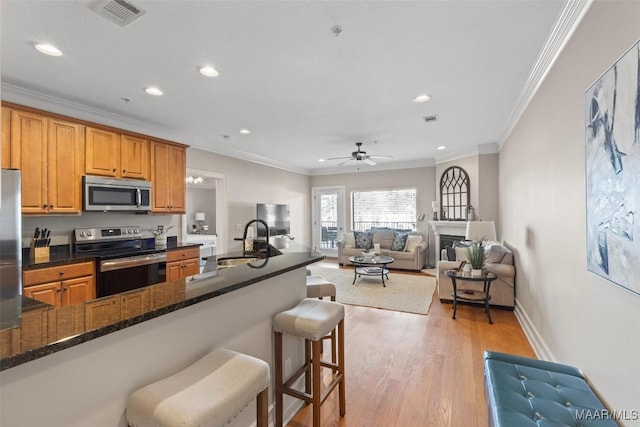 kitchen featuring sink, dark stone countertops, light hardwood / wood-style floors, stainless steel appliances, and crown molding