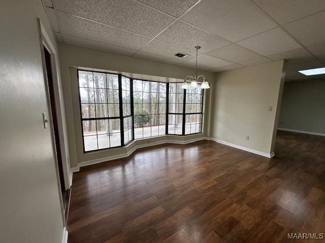 unfurnished dining area featuring a chandelier, a paneled ceiling, and dark hardwood / wood-style flooring