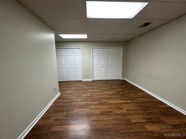 unfurnished bedroom featuring two closets, a paneled ceiling, and dark hardwood / wood-style floors