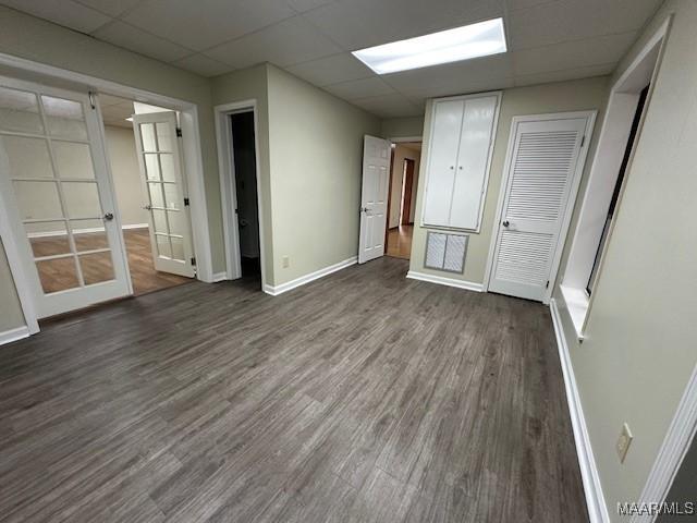 unfurnished bedroom featuring a drop ceiling, dark wood-type flooring, and french doors