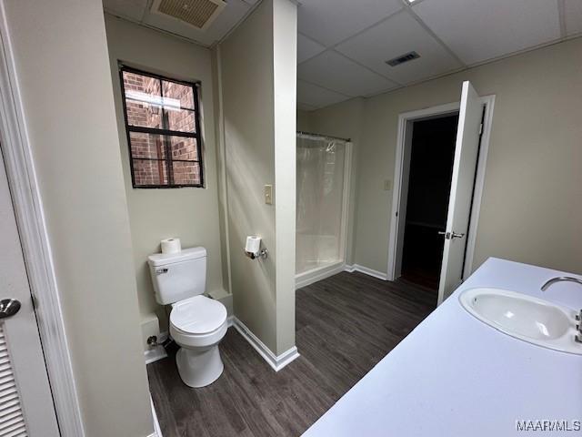 bathroom with hardwood / wood-style floors, vanity, walk in shower, toilet, and a drop ceiling