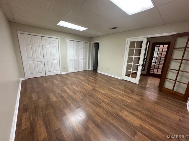 unfurnished bedroom with multiple closets, dark hardwood / wood-style floors, a drop ceiling, and french doors