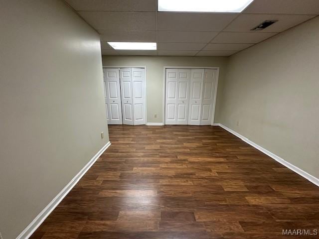 unfurnished bedroom featuring dark wood-type flooring, multiple closets, and a drop ceiling