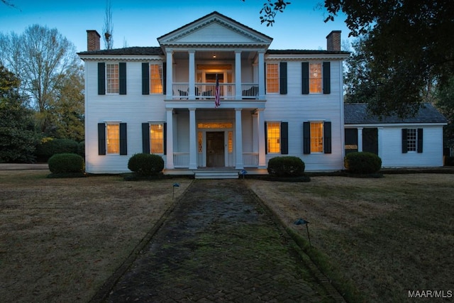 neoclassical / greek revival house featuring a balcony, an outdoor structure, and a front lawn