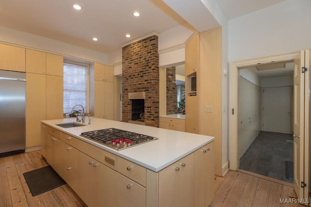 kitchen with sink, stainless steel appliances, light hardwood / wood-style floors, a center island with sink, and a brick fireplace