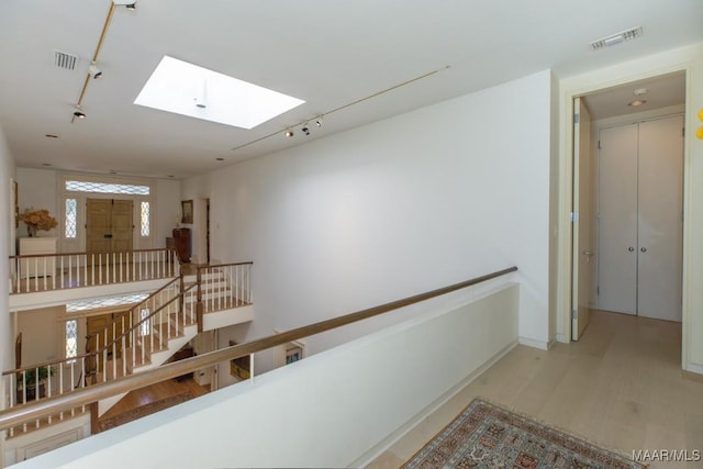 hallway featuring track lighting, a skylight, and light hardwood / wood-style flooring