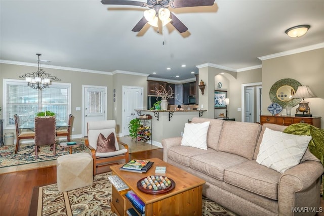 living room with ceiling fan with notable chandelier, wood-type flooring, and ornamental molding