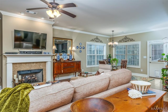 tiled living room with a tiled fireplace, crown molding, and ceiling fan with notable chandelier