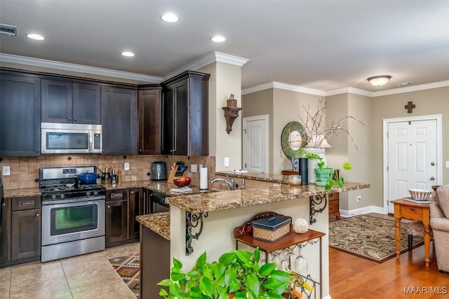 kitchen with stone countertops, dark brown cabinets, appliances with stainless steel finishes, kitchen peninsula, and backsplash