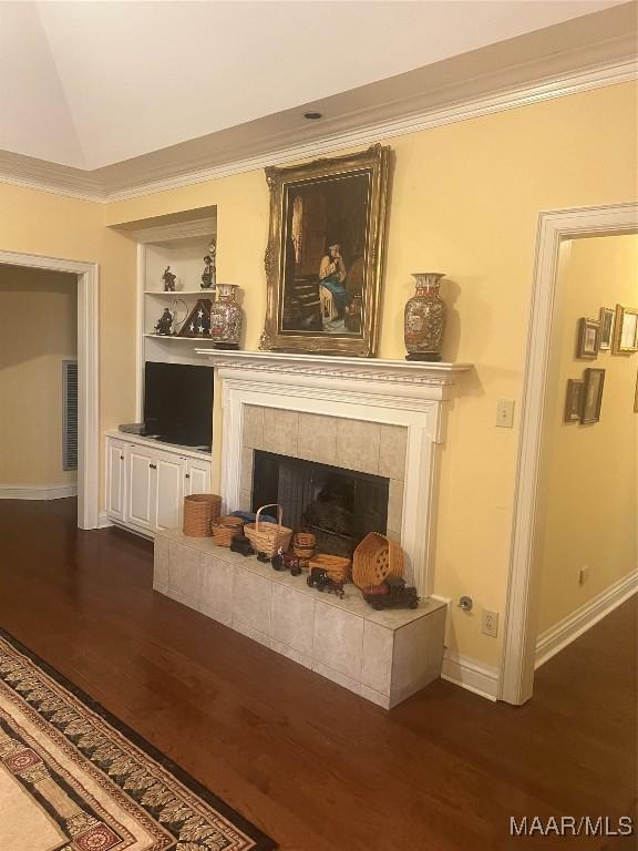 unfurnished living room with dark hardwood / wood-style floors, ornamental molding, a tiled fireplace, built in shelves, and vaulted ceiling