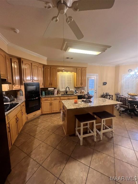 kitchen with sink, a kitchen breakfast bar, a center island, black appliances, and crown molding